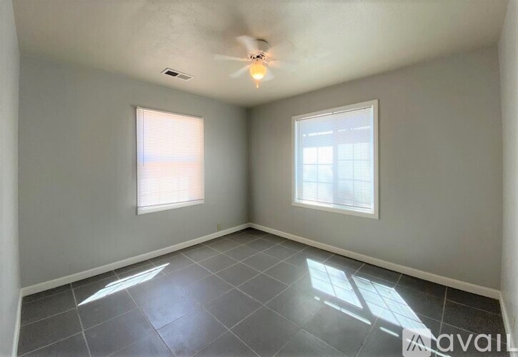A room with a ceiling fan and two windows.