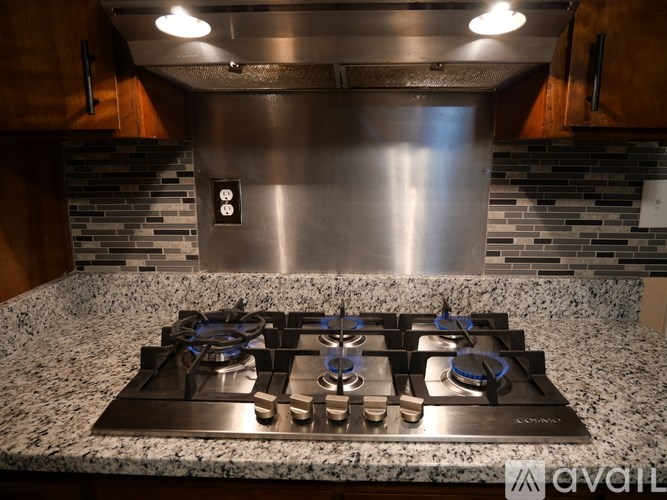 A modern kitchen with a granite countertop and a stainless steel gas stove.
