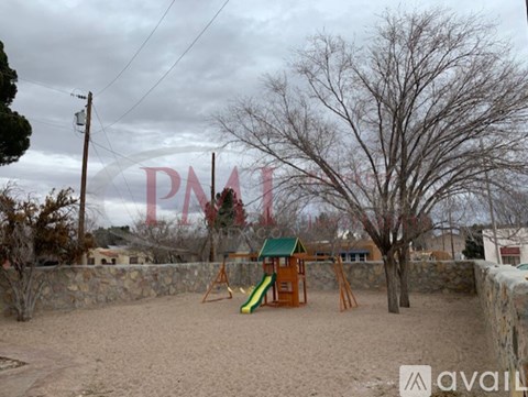 A playground with a slide and swings in a sandy area.