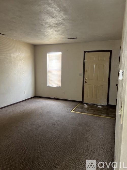 A room with a carpeted floor, a door, and a window with blinds.