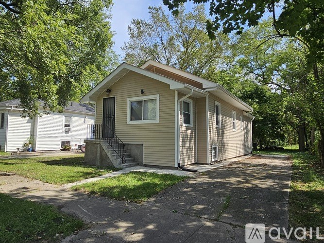 A small house with a brown roof and a white fence is surrounded by trees.