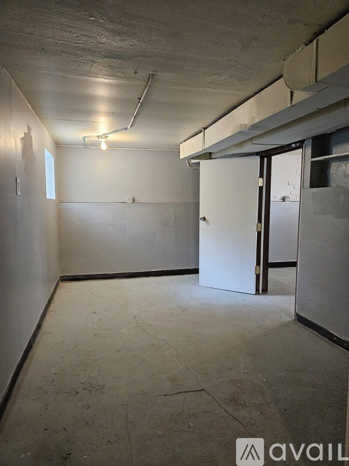A white door is on the right side of a room with a concrete floor and walls.