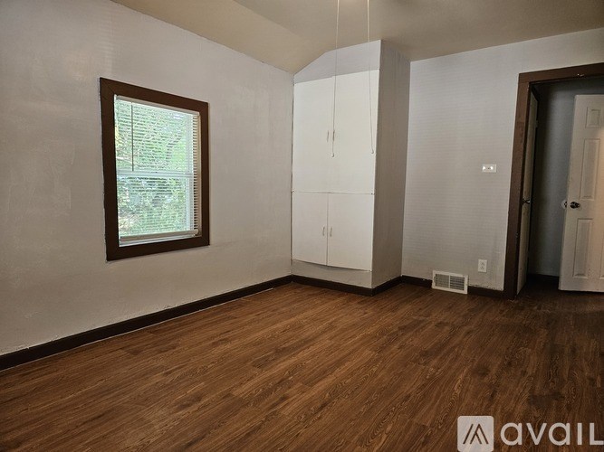 A room with wooden floors and white walls, with a window and a door on the right.