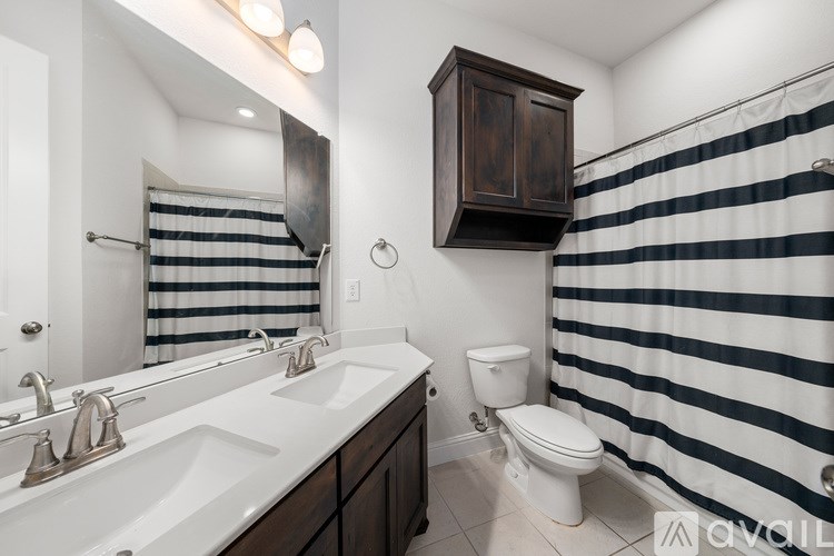 A bathroom with a striped shower curtain and a wooden cabinet above the toilet.