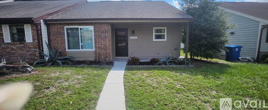 A small house with a brown brick exterior and a grey siding is shown with a white walkway leading to the front door.