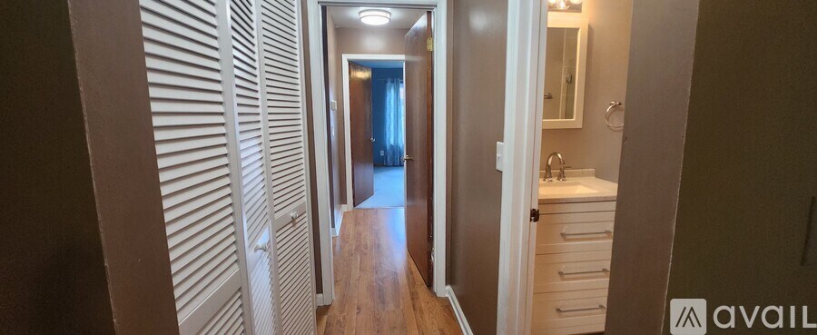 A hallway with a wooden floor and white walls leading to a bathroom.