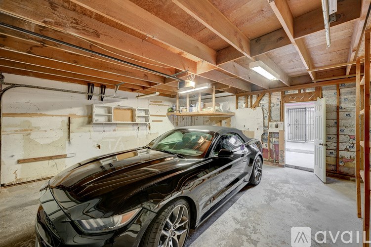 A black car is parked in a garage with wooden ceiling and walls.