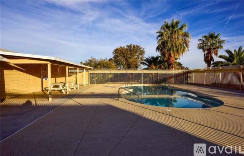 A pool surrounded by a concrete patio and a wooden house.
