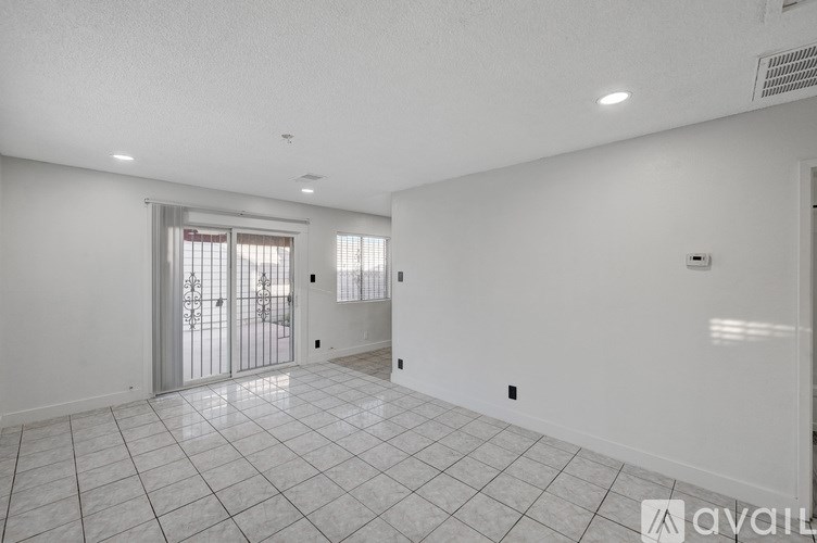 A spacious room with white walls and a tiled floor leading to a balcony.