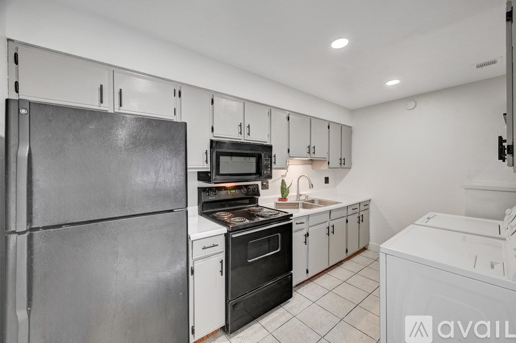 A kitchen with a black refrigerator, white cabinets, and a white dishwasher.