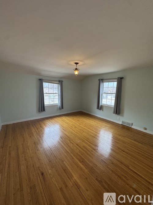 A room with wooden flooring and two windows.