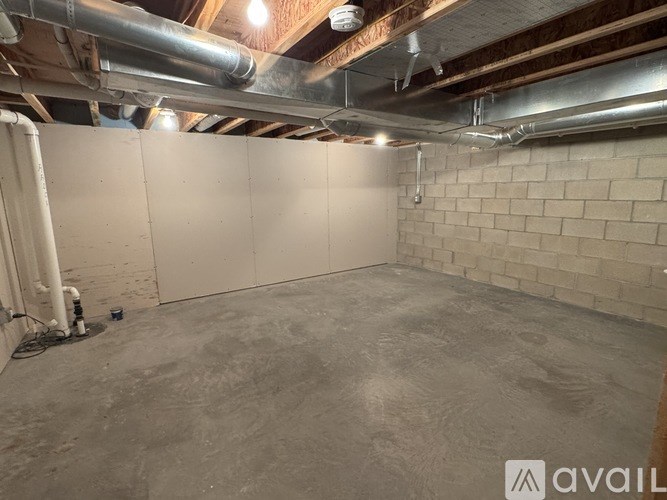 A room with a concrete floor and a brick wall with pipes running along the ceiling.