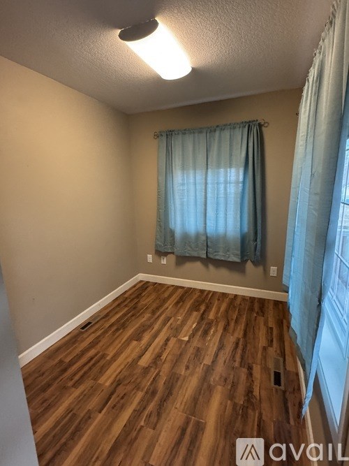 A room with wooden flooring and a window with blue curtains.