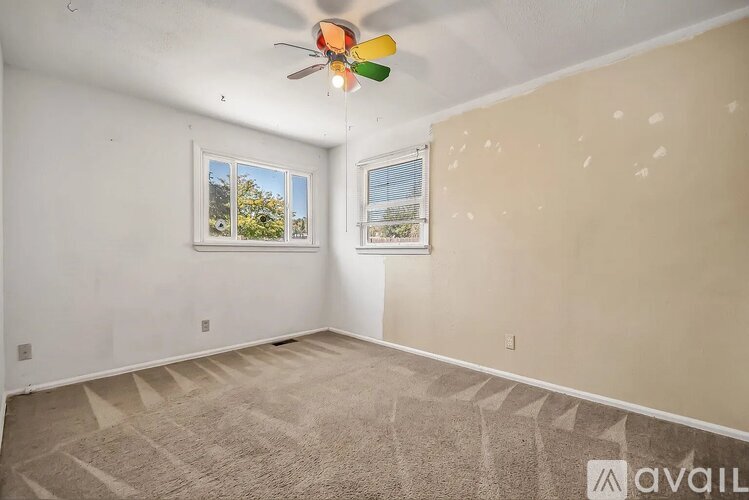 A room with a ceiling fan and two windows.