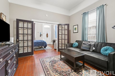A living room with a black couch and a rug.