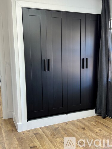 A black wardrobe with two doors and two handles is in a room with wooden flooring.