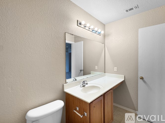 A bathroom with a white toilet, a sink, and a mirror with lights above it.