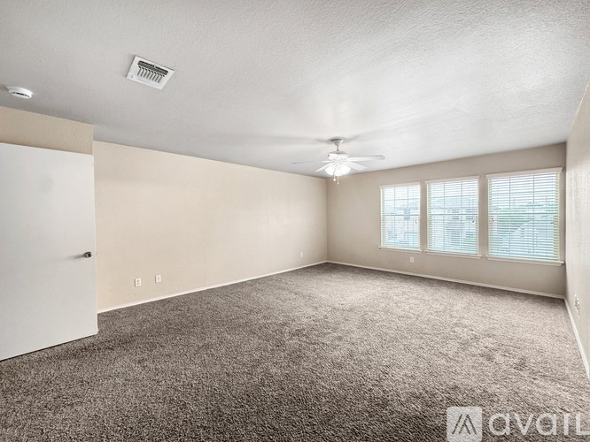 A spacious room with a carpeted floor, a ceiling fan, and a door leading to another room.