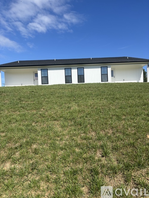 A white house with a black roof on a grassy hill.