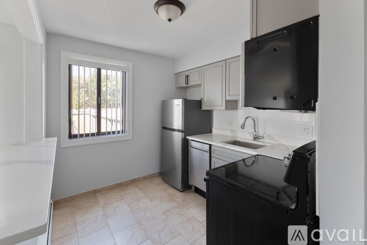 A kitchen with a black fridge, white cabinets, and a window with blinds.