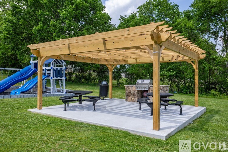 A wooden pergola with a picnic table and a slide in the background.