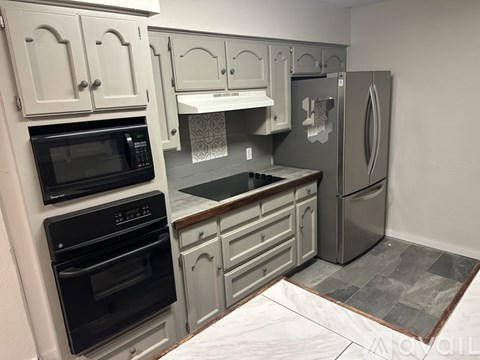 A kitchen with a black oven and microwave, a refrigerator, and a countertop with a sink.