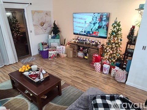 A living room with a television on, a coffee table in the middle and a Christmas tree in the corner.