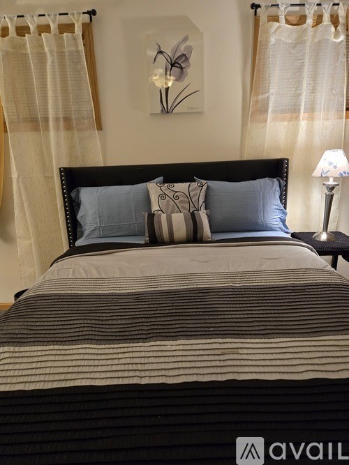 A bed with a striped comforter and two striped pillows sits in a room with a white wall and a framed picture of a flower.