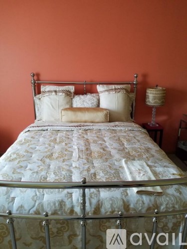 A bed with a metal frame and a patterned bedspread sits against an orange wall.