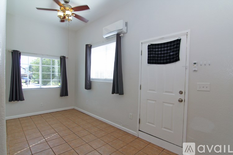 A room with a ceiling fan, two windows with curtains, and a door.