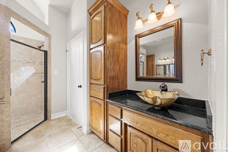 A bathroom with a wooden cabinet, a black countertop, and a large mirror.