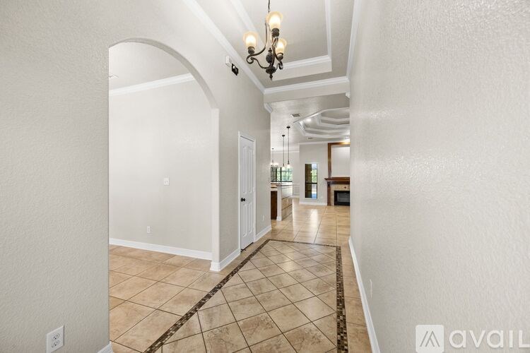 A long hallway with a chandelier and tiled flooring.