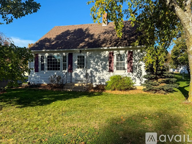 A white house with a brown roof and a tree in front.