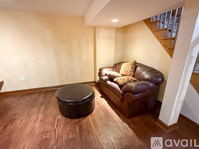 A brown leather couch with a black ottoman in a room with wooden flooring.