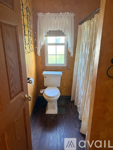 A small bathroom with a toilet, a window, and a wooden door.