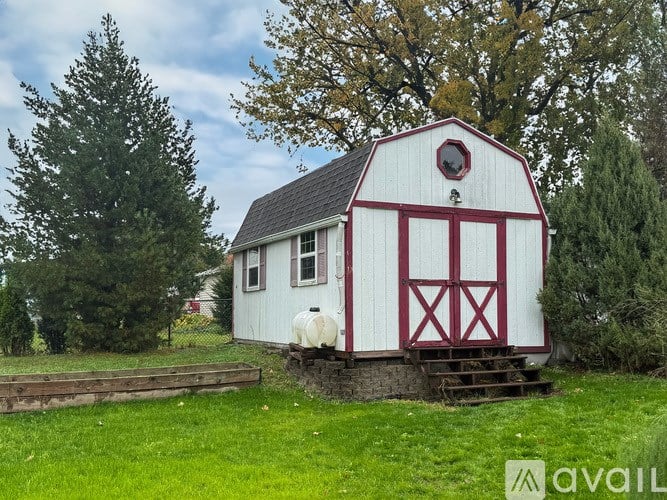 A white barn with a red door and windows sits in a grassy field.