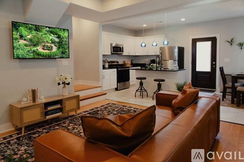 A living room with a brown leather couch and a television displaying a forest scene.