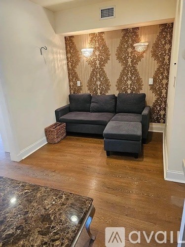A grey couch with a matching ottoman in front of a patterned wallpapered wall.