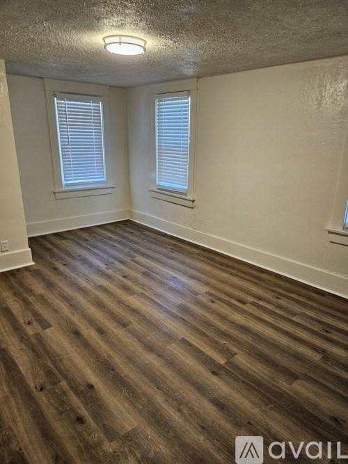 A room with wooden flooring and two windows.