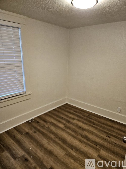 A room with wooden flooring and a window with blinds.