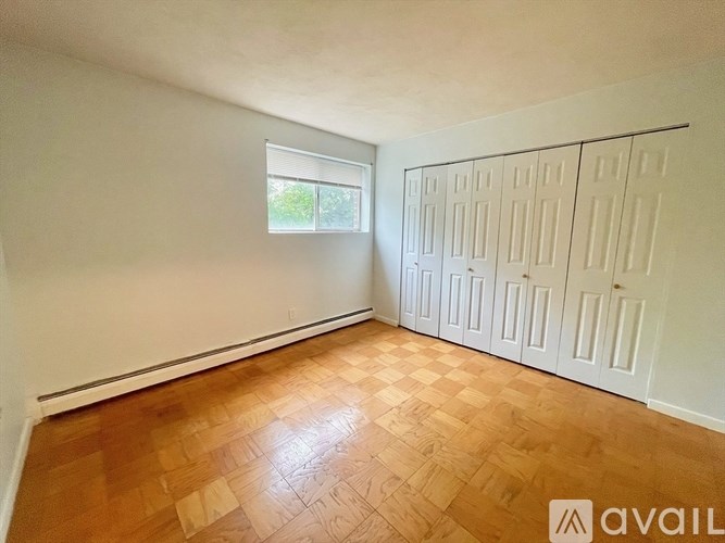 A room with wooden flooring and white walls, with a window and a row of cupboards.