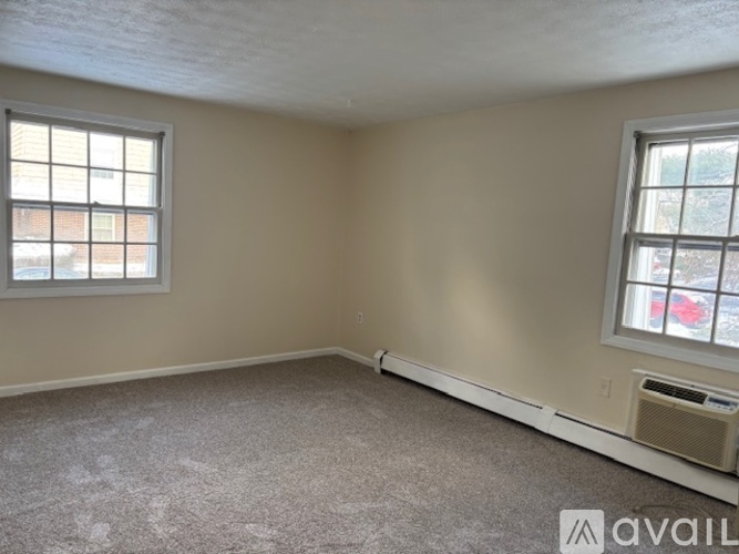 A room with a carpeted floor, two windows, and a wall-mounted air conditioning unit.
