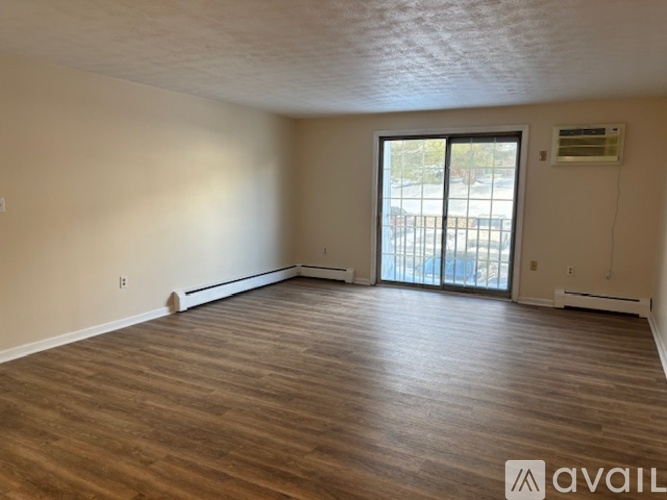 A spacious room with wooden flooring and a sliding glass door leading to a balcony.