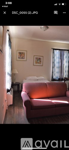 A red couch is in the foreground of a room with a white bed and a painting on the wall.