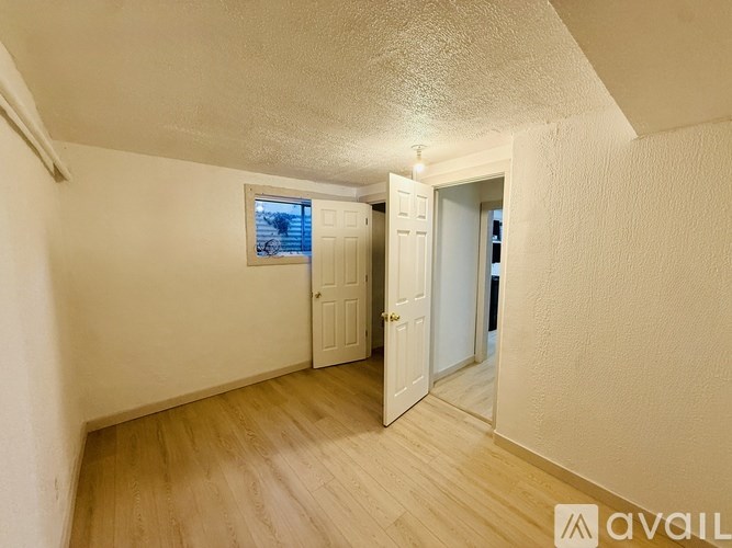 A room with wooden flooring and a window with a view of a fence and trees.