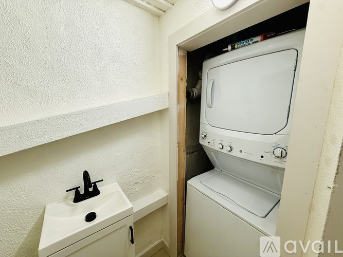 A small white sink with a black faucet is next to a white washing machine in a small room.