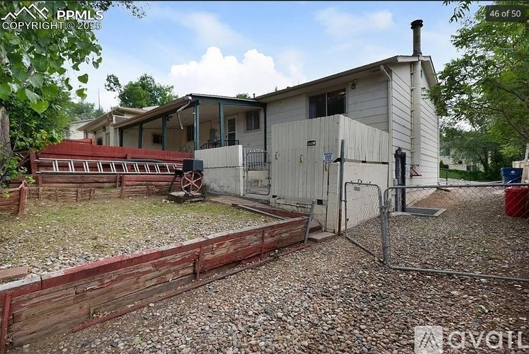 A house with a white exterior and a red roof is surrounded by a gravel area and a wooden fence.