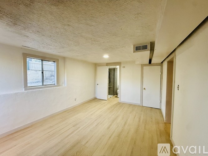A room with wooden flooring and a window with a view of a building outside.