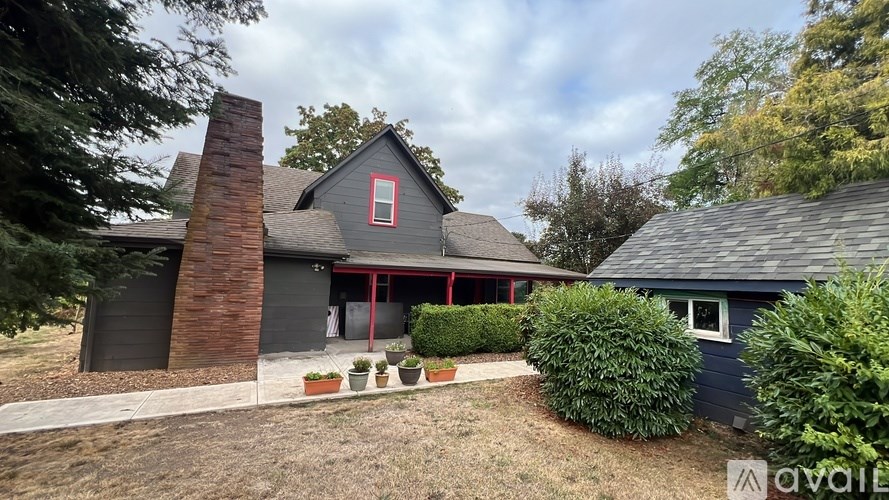 A house with a red window and a chimney is surrounded by greenery.