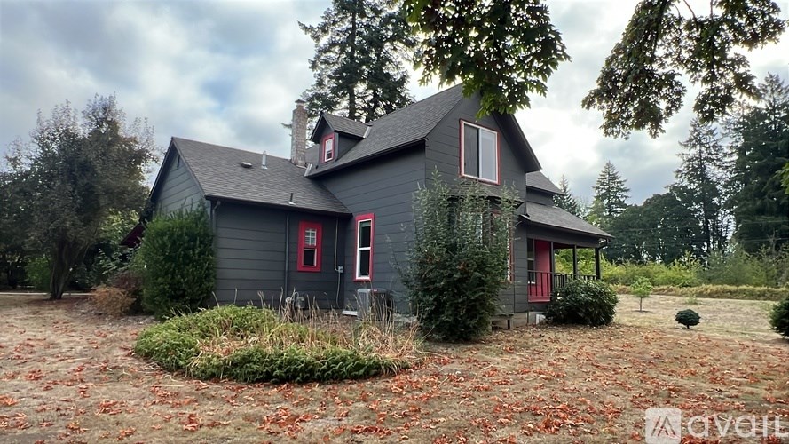A grey house with red doors and windows surrounded by trees.